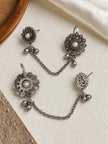 Two pairs of oxidised silver floral ear cuff studs with pearl centres, ghungroo drops, and linking chains laid flat on white surface