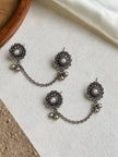 Two pairs of oxidised silver pearl floral ear cuff stud sets with ghungroo drops and chains displayed on white textured surface