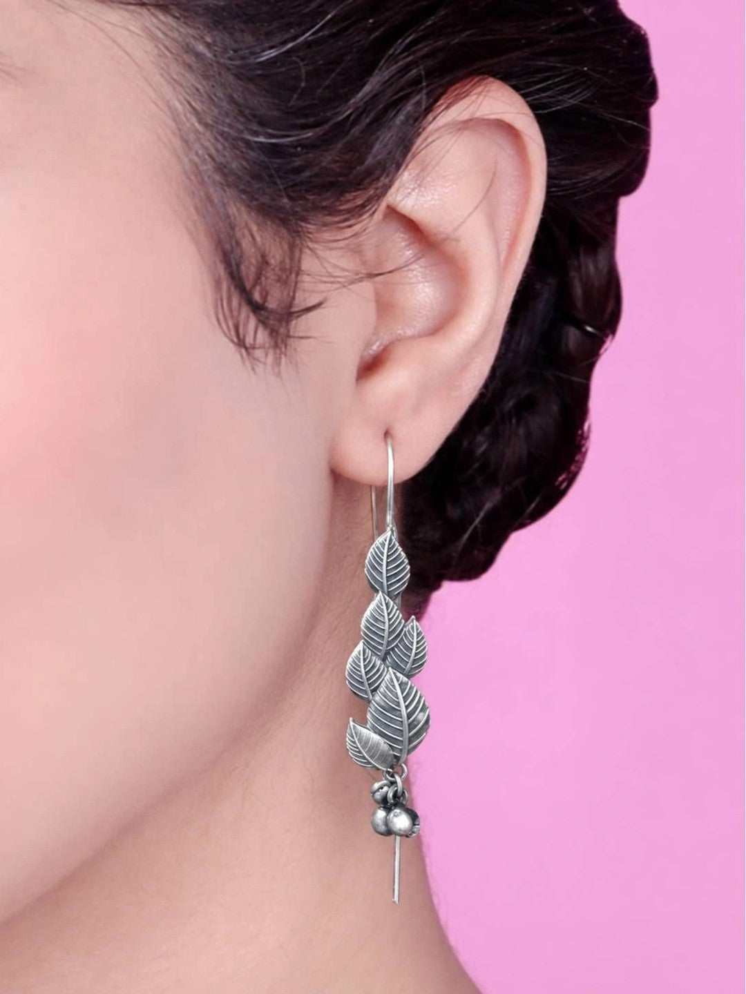 Oxidised silver cascading leaf drop earring worn on a woman's ear against a pink background