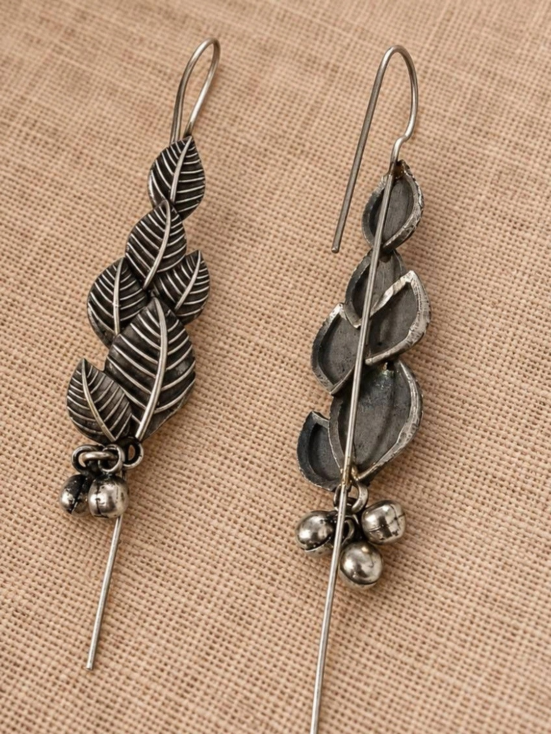 Front and back view of oxidised silver leaf earrings showing threader hook and ghungroo bells on linen