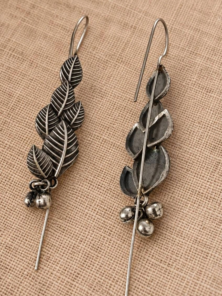 Front and back view of oxidised silver leaf earrings showing threader hook and ghungroo bells on linen