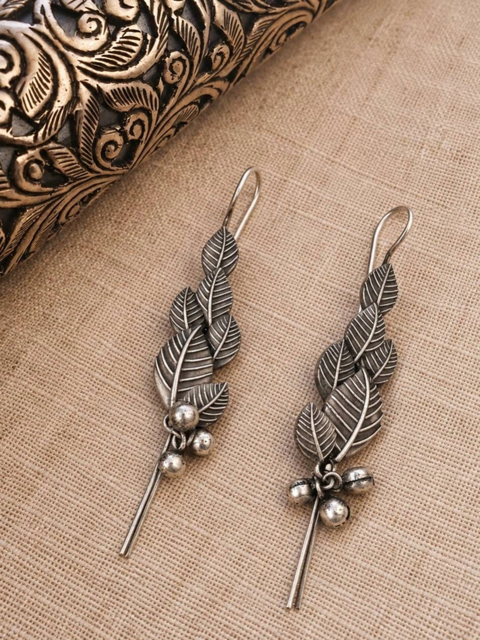 Pair of oxidised silver leaf earrings with ghungroo bells laid flat on linen beside a carved box
