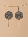 Pair of oxidised silver karma coin drop earrings hanging on a jute rope against a beige background