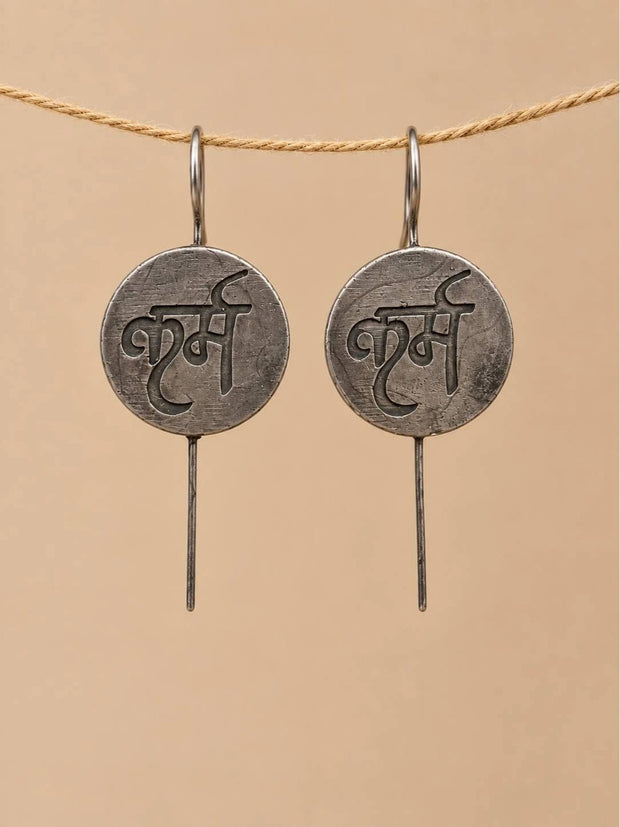 Pair of oxidised silver karma coin drop earrings hanging on a jute rope against a beige background