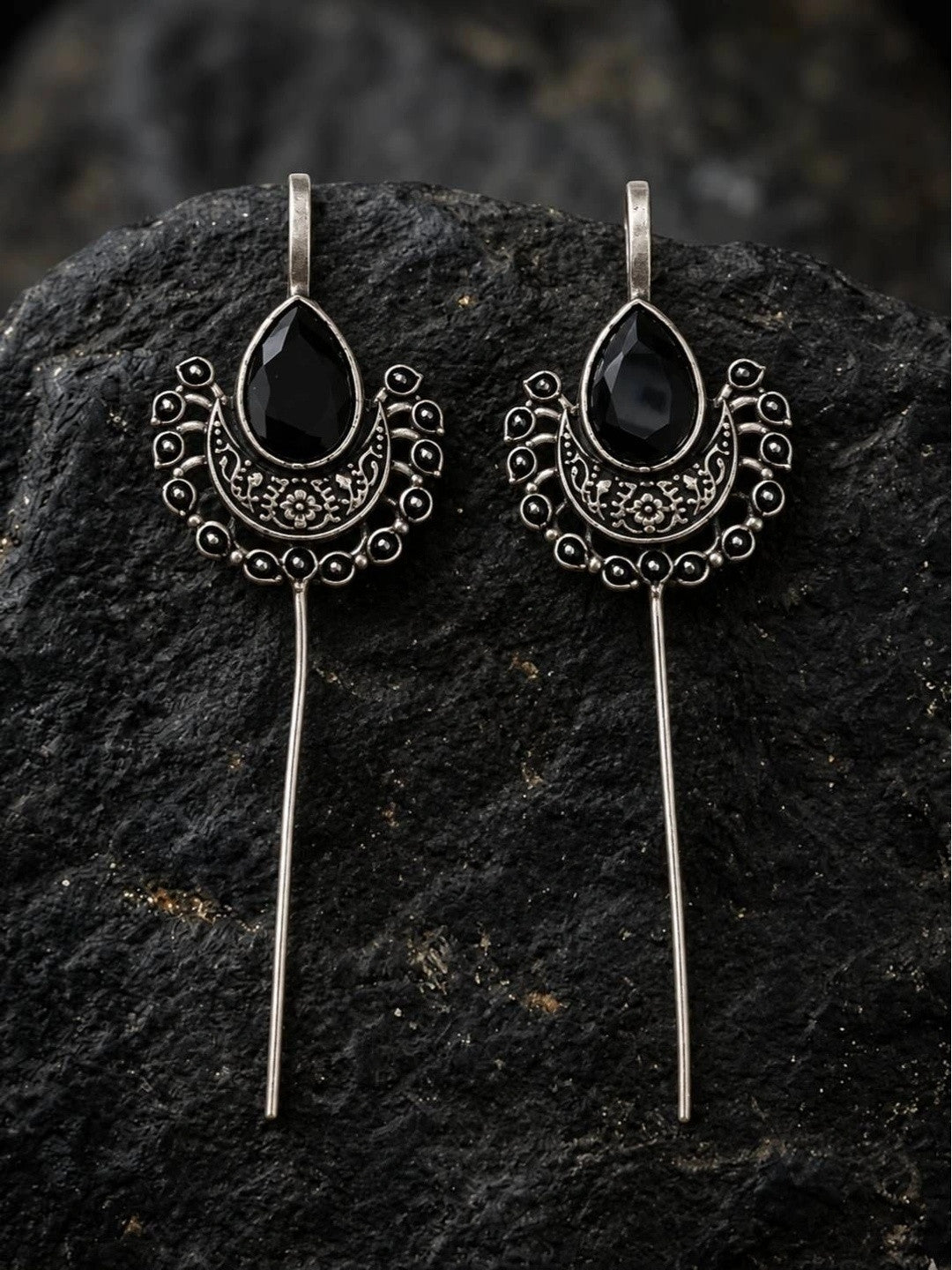 Pair of oxidised silver ear cuff earrings with black stone displayed on dark textured rock surface