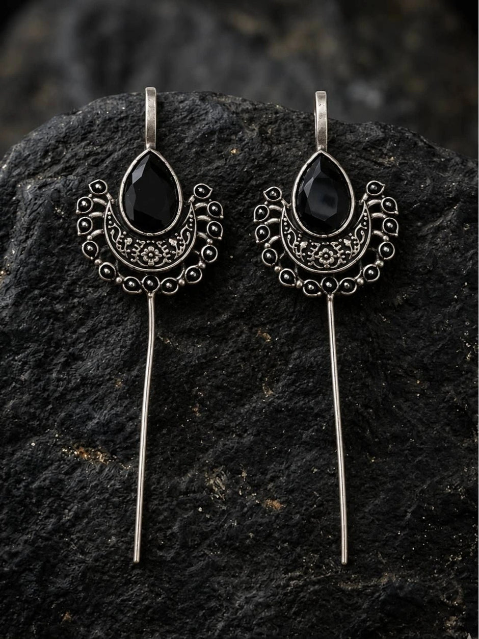 Pair of oxidised silver ear cuff earrings with black stone displayed on dark textured rock surface