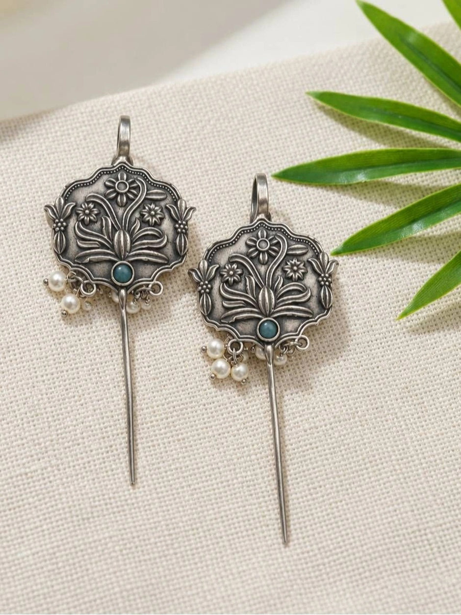 Pair of oxidised silver floral ear cuff earrings with turquoise stone and pearl drops on white fabric