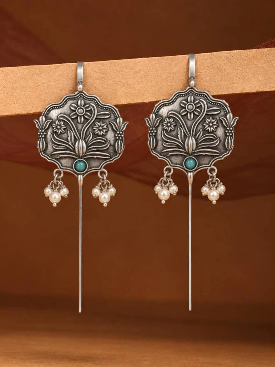 Two oxidised silver floral ear cuff earrings hanging against a warm terracotta background