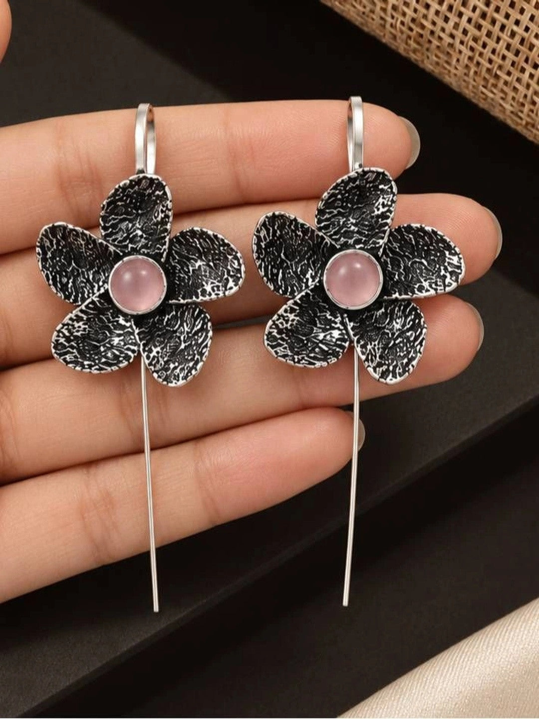 Pair of oxidised silver floral ear cuff earrings with pink cabochon centres held in an open palm