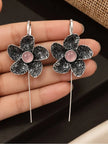 Pair of oxidised silver floral ear cuff earrings with pink cabochon centres held in an open palm