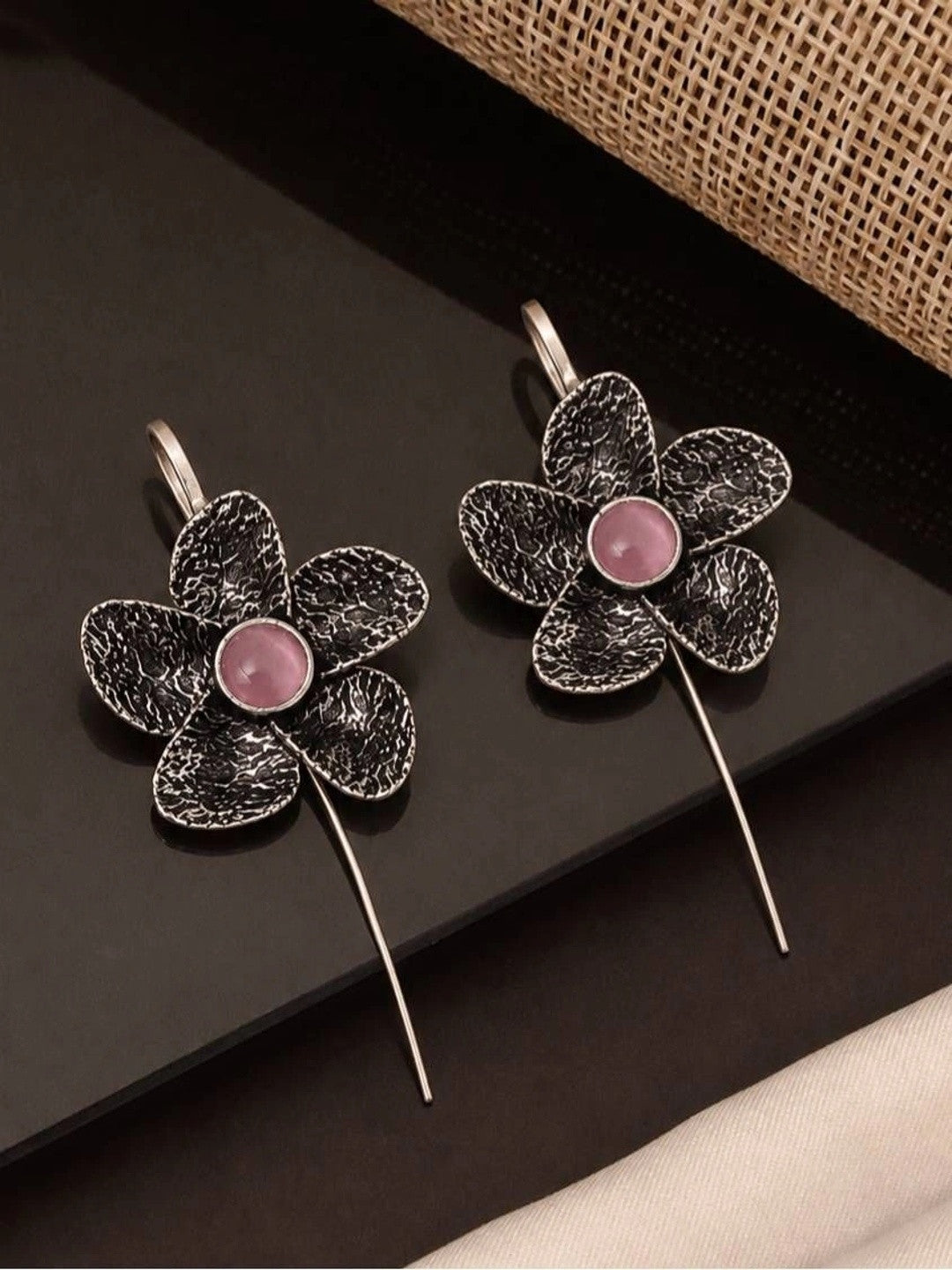Two oxidised silver floral ear cuff earrings with pink stone centres laid flat on a dark surface