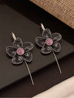 Two oxidised silver floral ear cuff earrings with pink stone centres laid flat on a dark surface