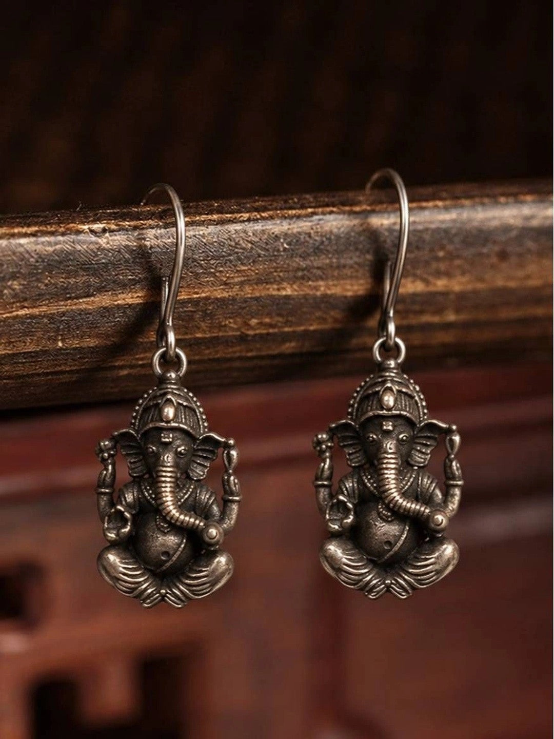 Pair of oxidised silver Ganesha drop earrings hanging from a dark wooden rail