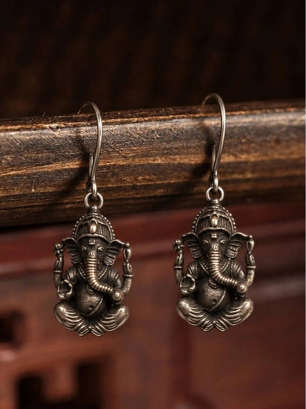 Pair of oxidised silver Ganesha drop earrings hanging from a dark wooden rail