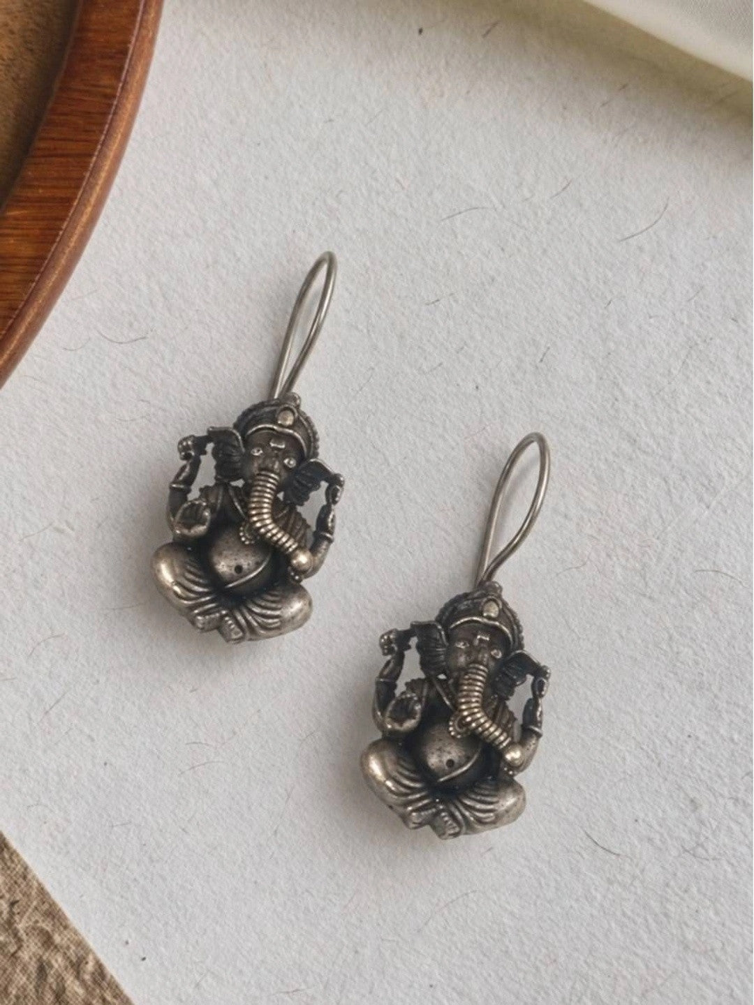 Two oxidised silver Ganesha earrings placed side by side on a white textured surface