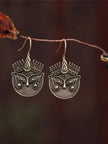 Pair of oxidised silver Durga face drop earrings hanging from a dried branch against a dark background