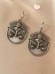 Two oxidised silver Durga face earrings with crown and eye detailing laid flat on a cream surface