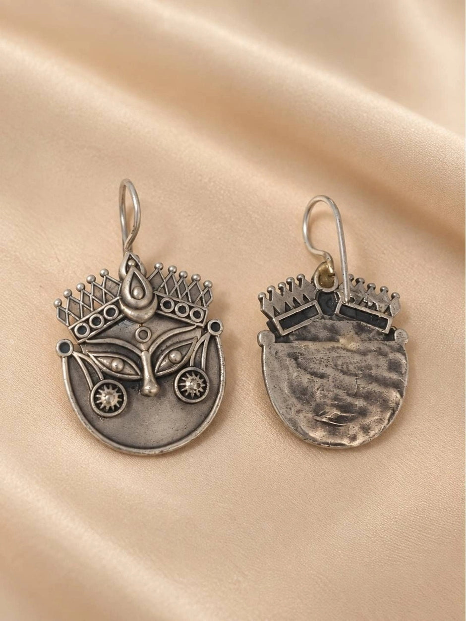 Front and back view of a single oxidised silver Durga face earring showing textured reverse side on silk fabric