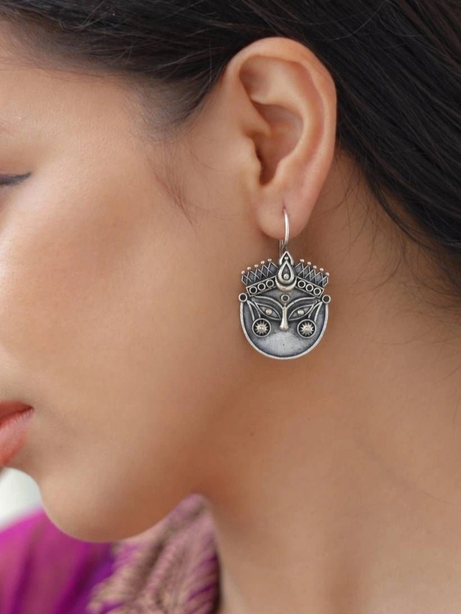 Woman wearing an oxidised silver Durga face drop earring with a purple outfit shown in close profile