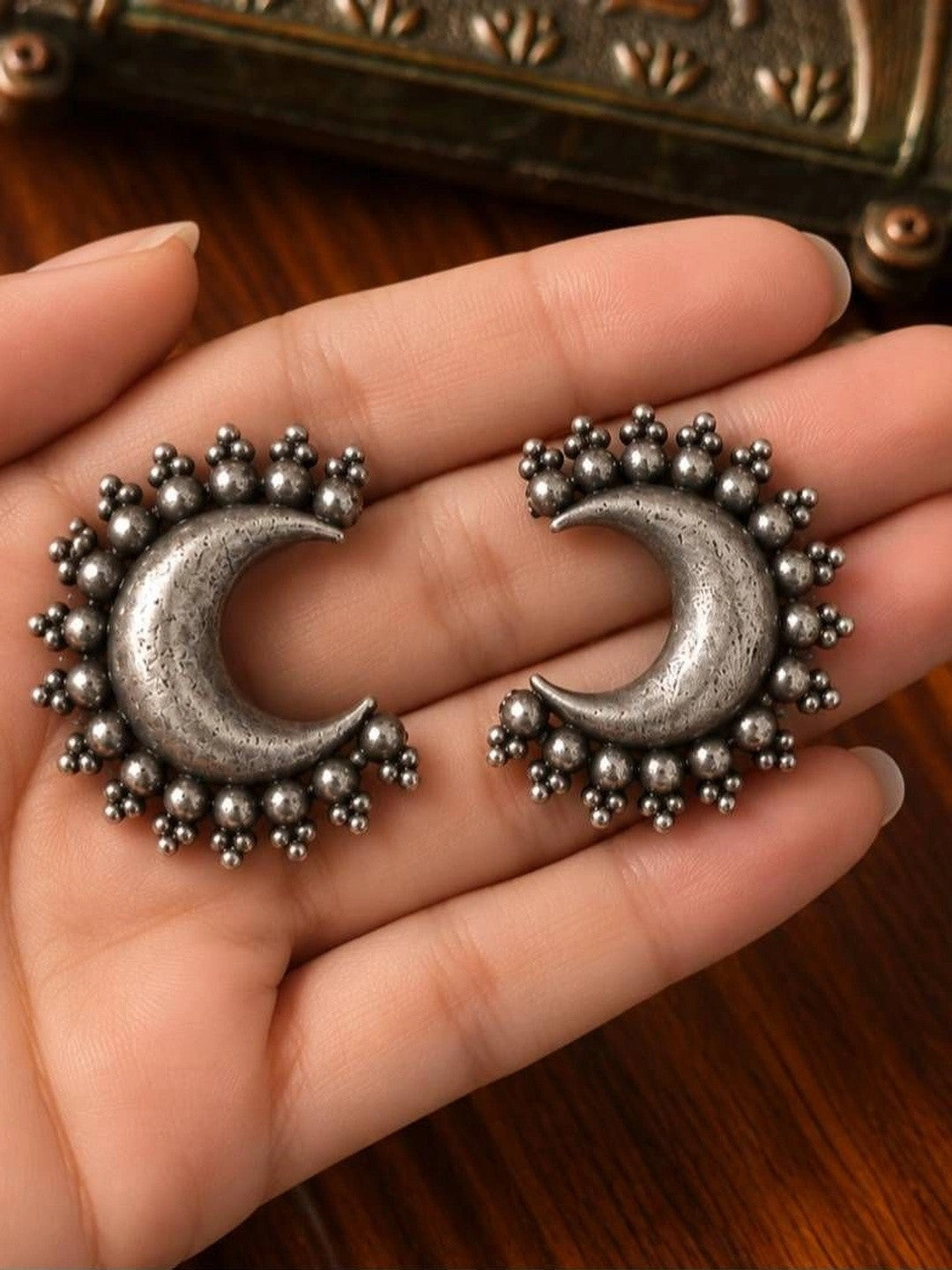 Pair of oxidised silver crescent moon stud earrings with granule bead border held in a woman's open palm