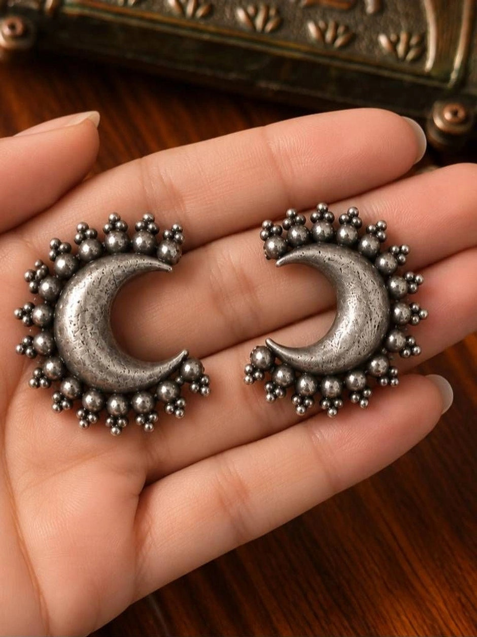 Pair of oxidised silver crescent moon stud earrings with granule bead border held in a woman's open palm