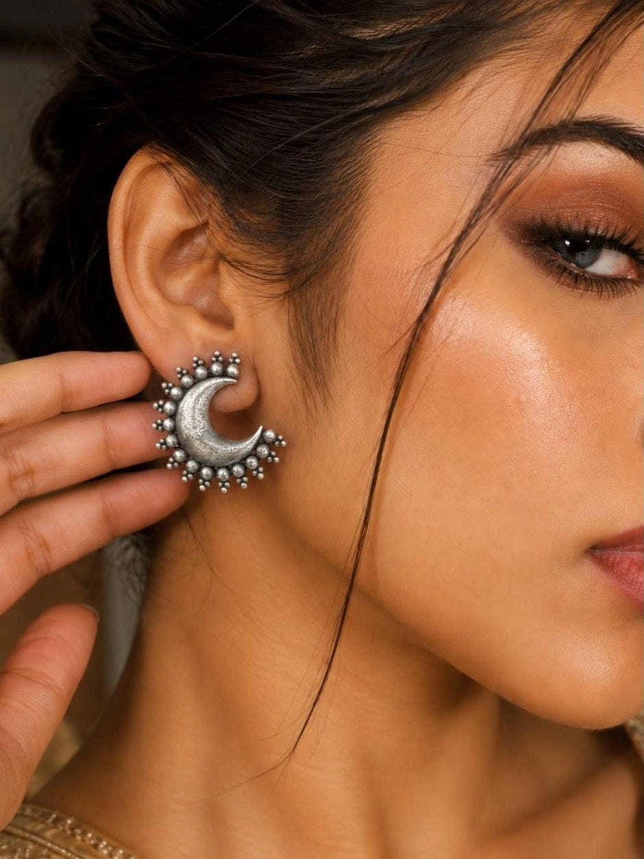 Close-up of a woman wearing an oxidised silver crescent moon stud earring, showing fit and scale on the ear