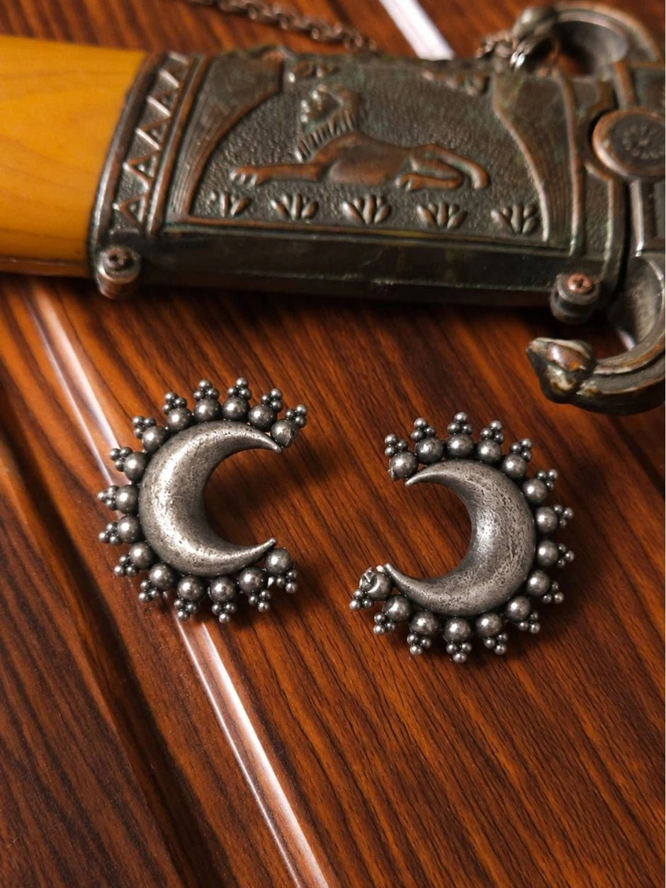 Both oxidised silver crescent moon stud earrings laid flat on a wooden surface next to an engraved silver jewellery box