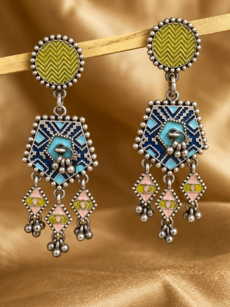 Pair of oxidised silver geometric drop earrings with olive enamel studs, navy tribal pentagon and pink diamond dangles on golden fabric