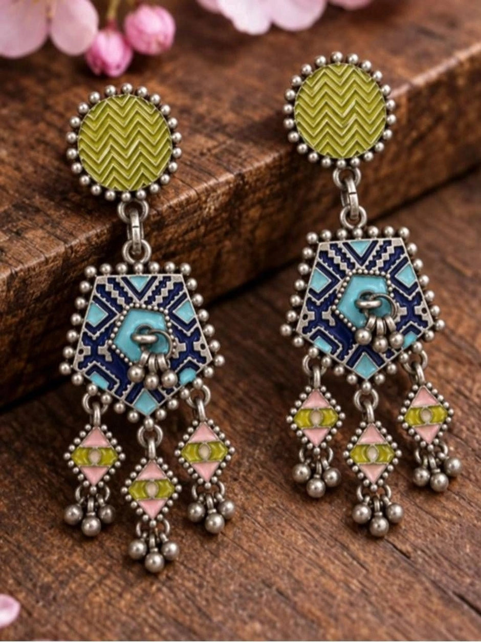 Both geometric drop earrings laid flat on wooden surface showing olive chevron tops and multicolour enamel pendants