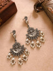 Pair of oxidised silver chandbali earrings with pearl cluster drops laid flat on beige surface near wooden boxes