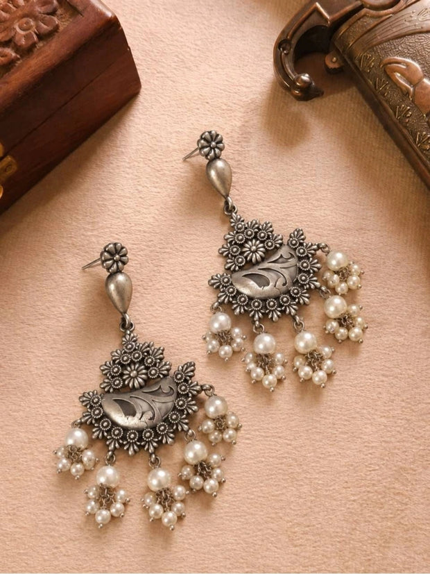 Pair of oxidised silver chandbali earrings with pearl cluster drops laid flat on beige surface near wooden boxes
