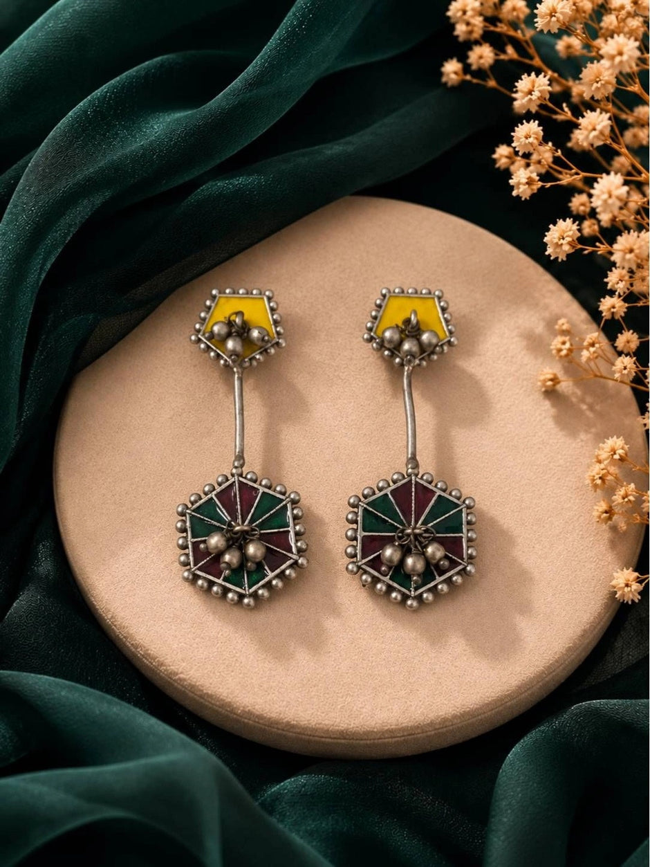 Pair of oxidised silver enamel drop earrings with hexagonal teal and maroon pendant on beige display tray