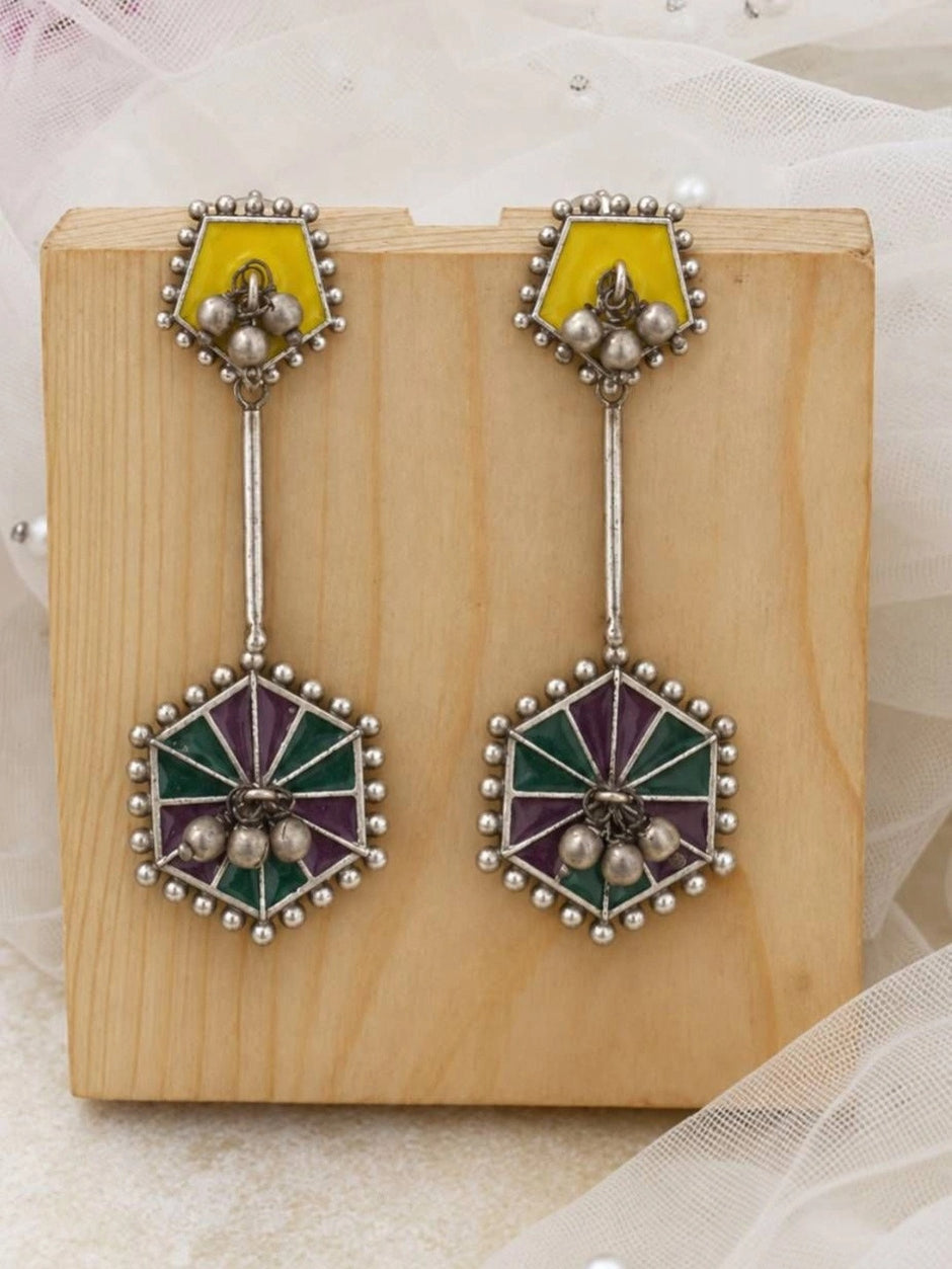 Oxidised silver geometric drop earrings with yellow pentagon studs and teal purple enamel hexagonal pendants on wooden block