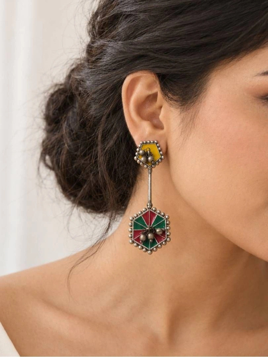 Woman wearing oxidised silver geometric drop earring with yellow stud and red green enamel hexagonal pendant