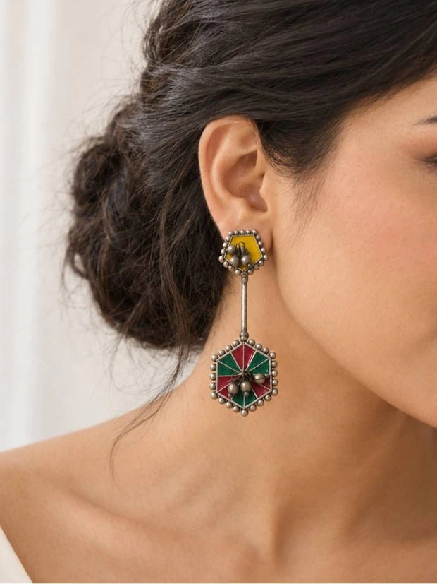 Woman wearing oxidised silver geometric drop earring with yellow stud and red green enamel hexagonal pendant