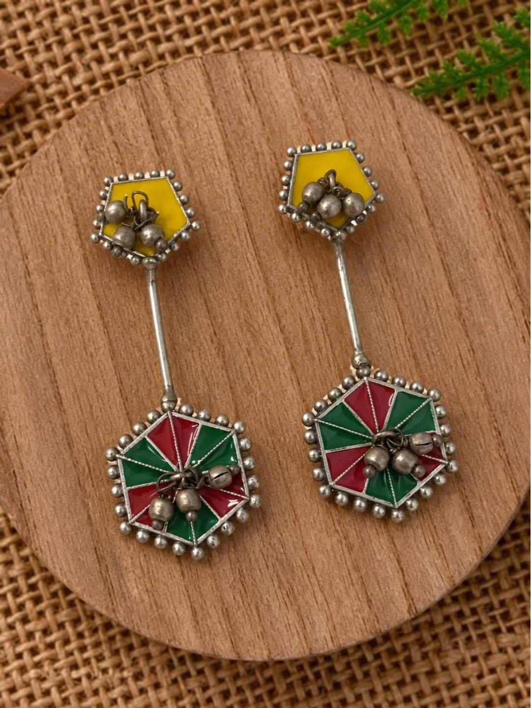 Pair of oxidised geometric enamel drop earrings with ghungroo bells displayed on a round wooden surface