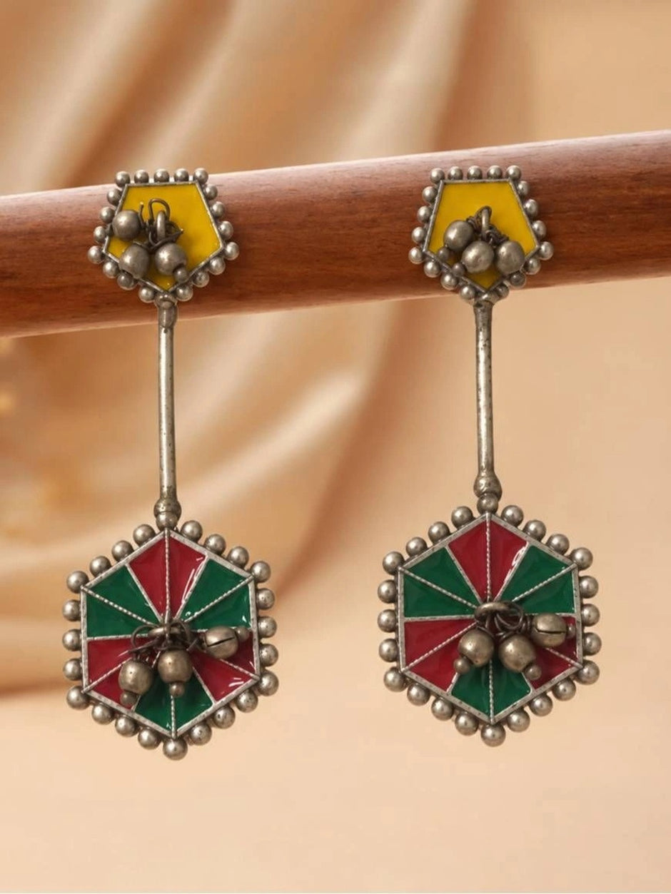 Front view of oxidised silver enamel earrings with red and green hexagonal pendant hanging on a wooden rod