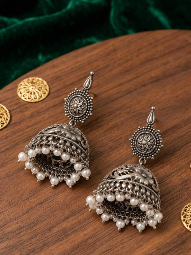 Pair of oxidised silver filigree jhumka earrings with pearl fringe laid on wooden surface