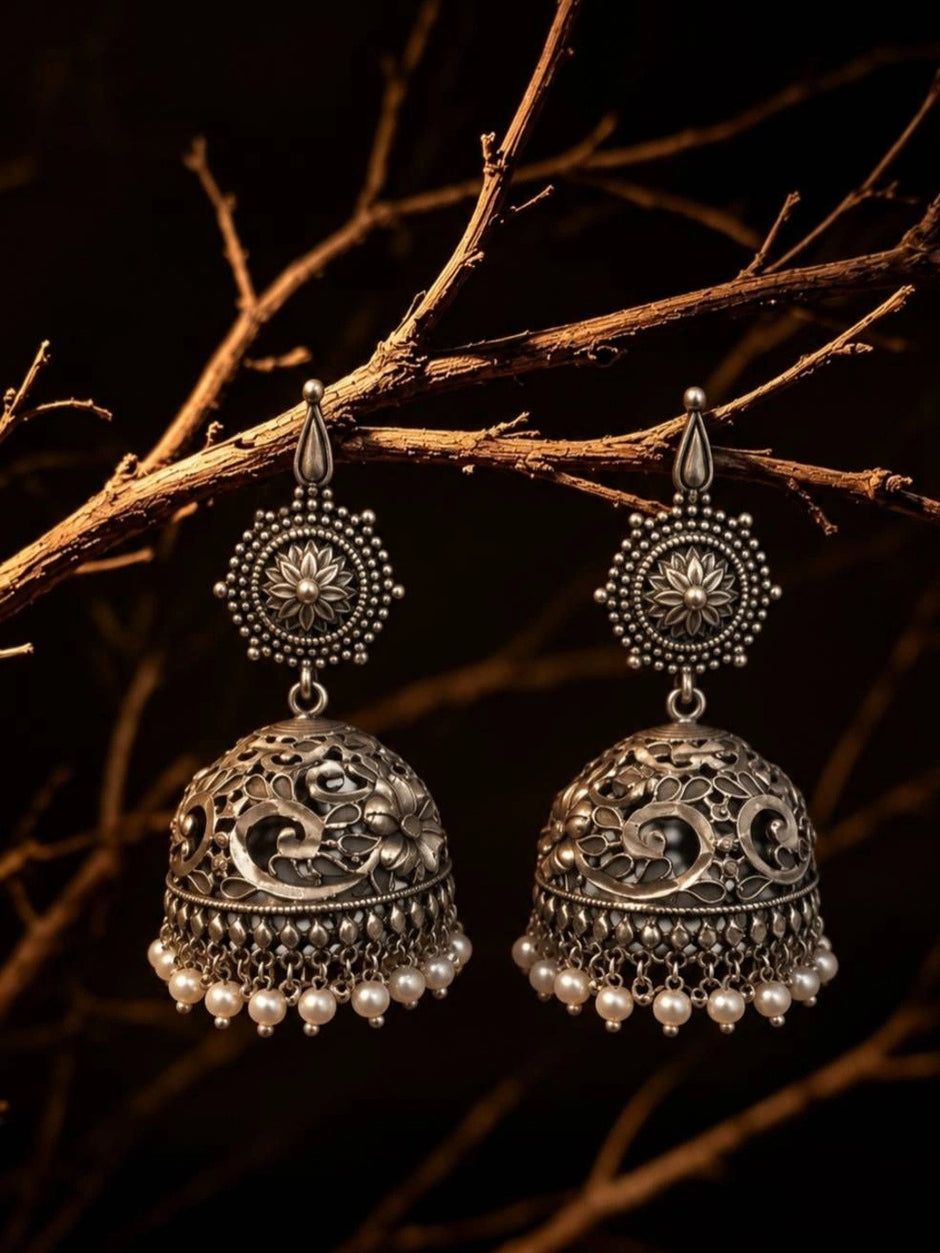 Oxidised silver jhumka earring pair with pearl drops displayed on rustic branch in dramatic lighting