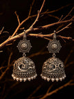 Oxidised silver jhumka earring pair with pearl drops displayed on rustic branch in dramatic lighting