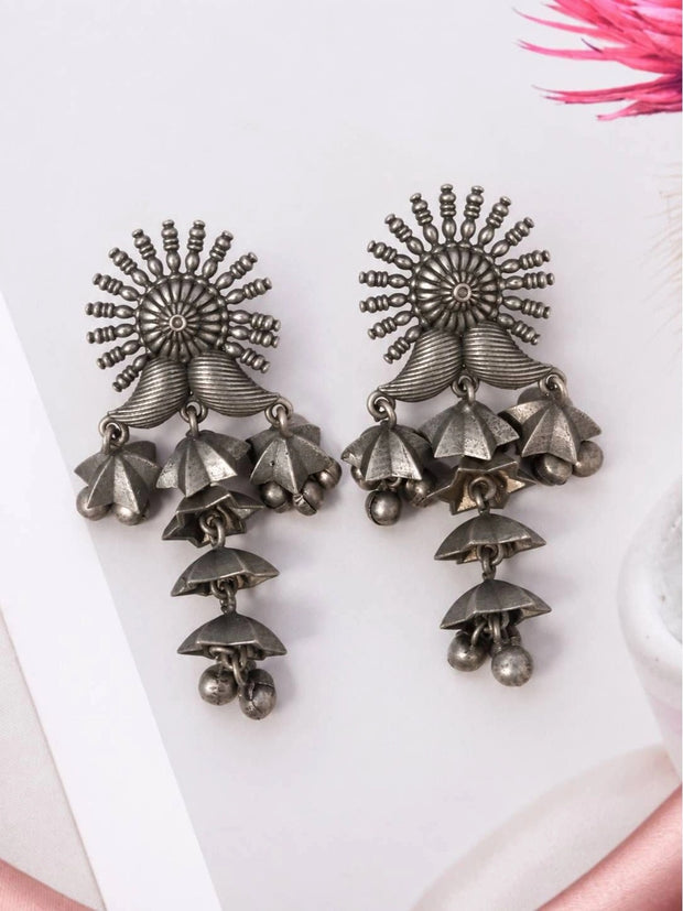 Pair of oxidised silver cascading jhumka earrings with sun-burst tops and tiered umbrella drops laid flat on white surface