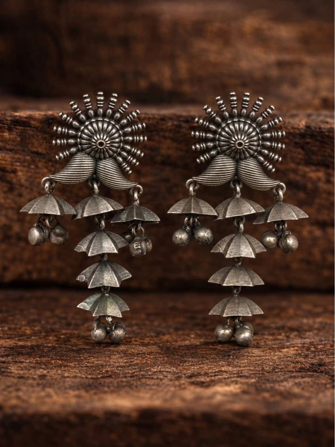 Pair of oxidised silver tiered jhumka earrings displayed on a dark wooden surface showing cascading umbrella tiers