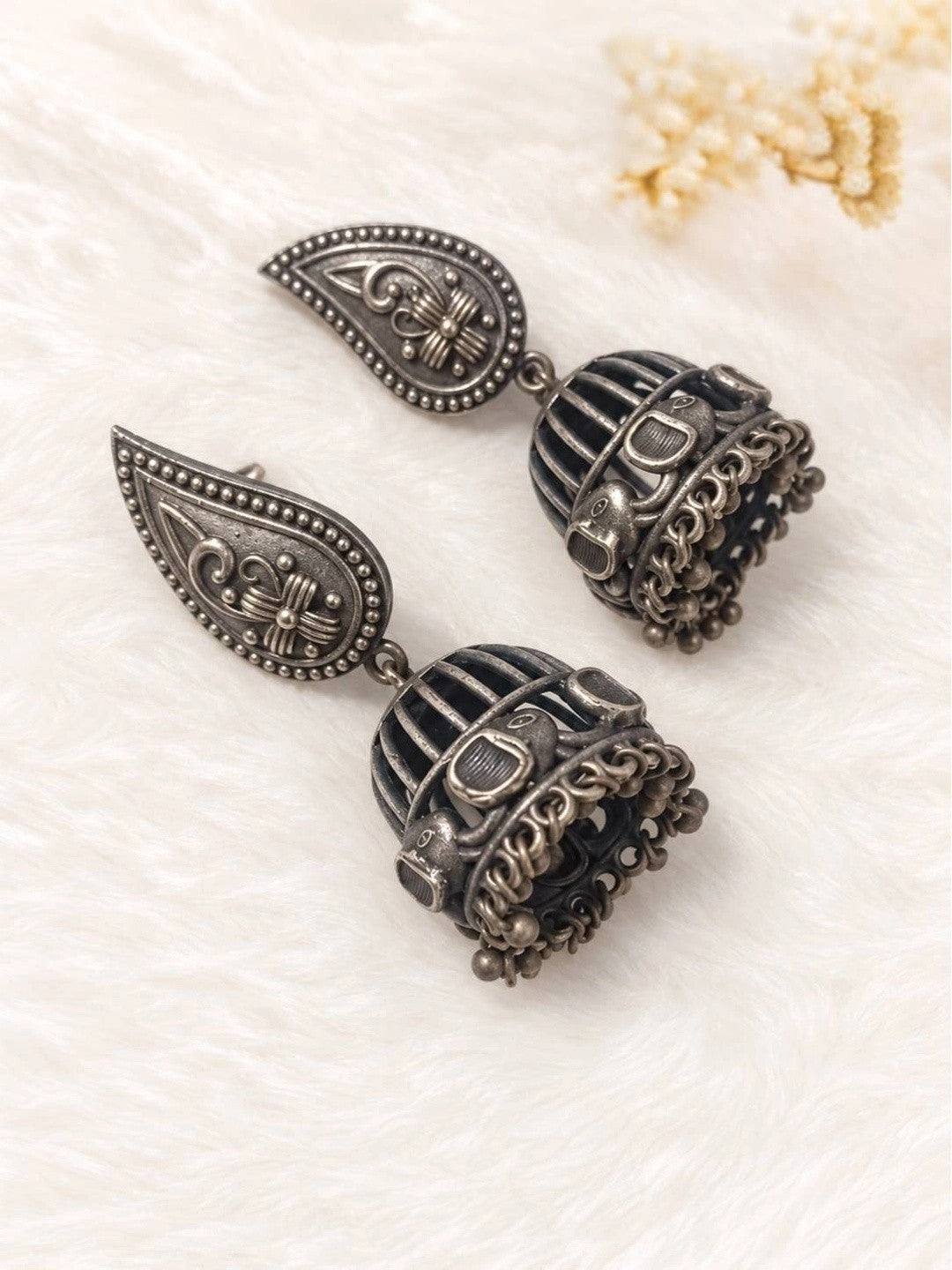 Pair of oxidised silver birdcage jhumka earrings with bird motifs placed on white fur surface