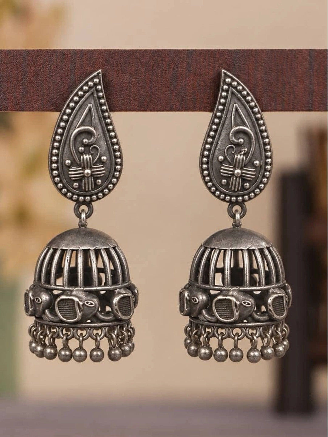 Pair of oxidised silver paisley jhumka earrings with ghungroo drops displayed on wooden surface