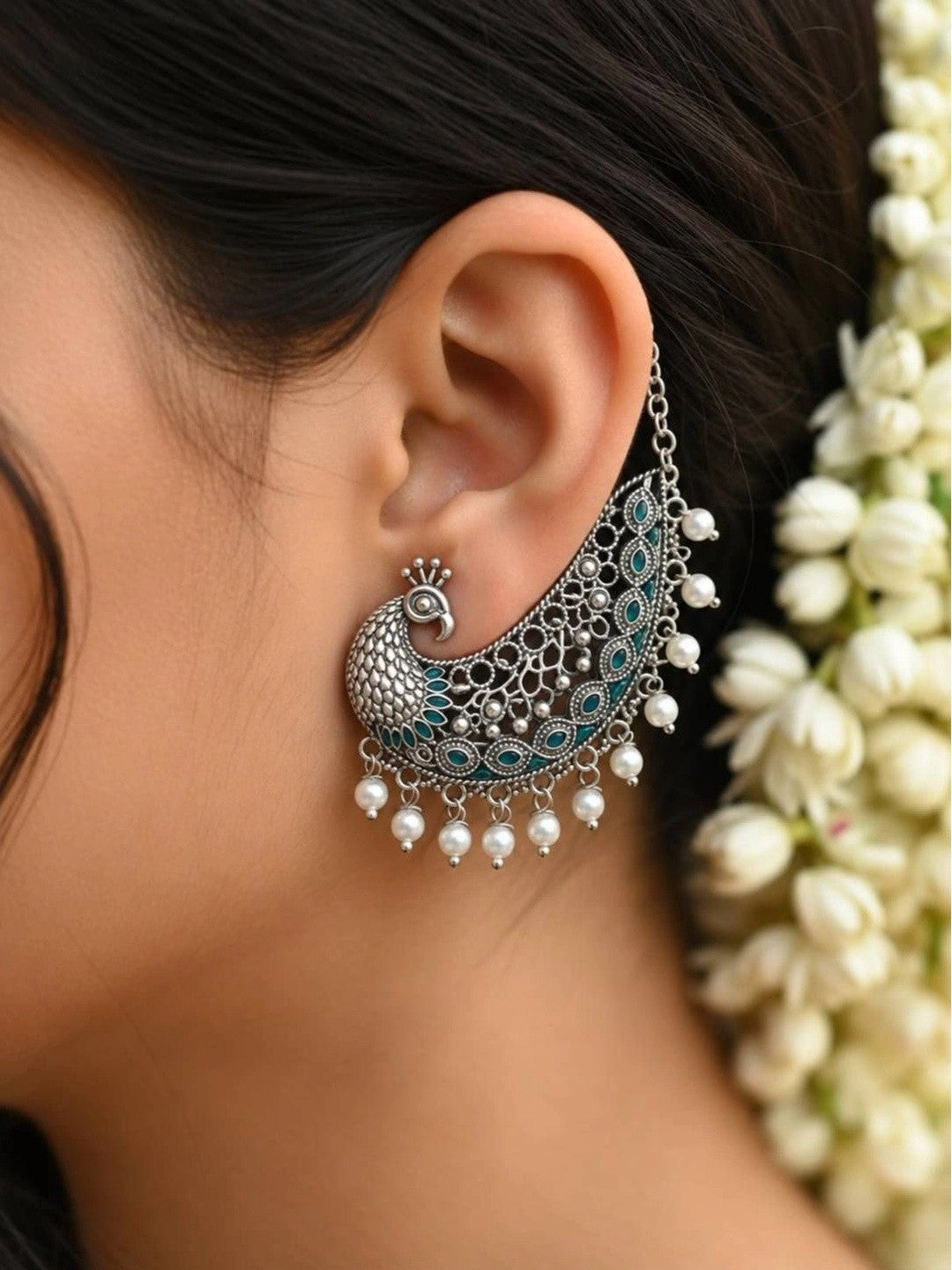 Close-up of peacock ear cuff worn on a woman's ear with jasmine flowers in her hair