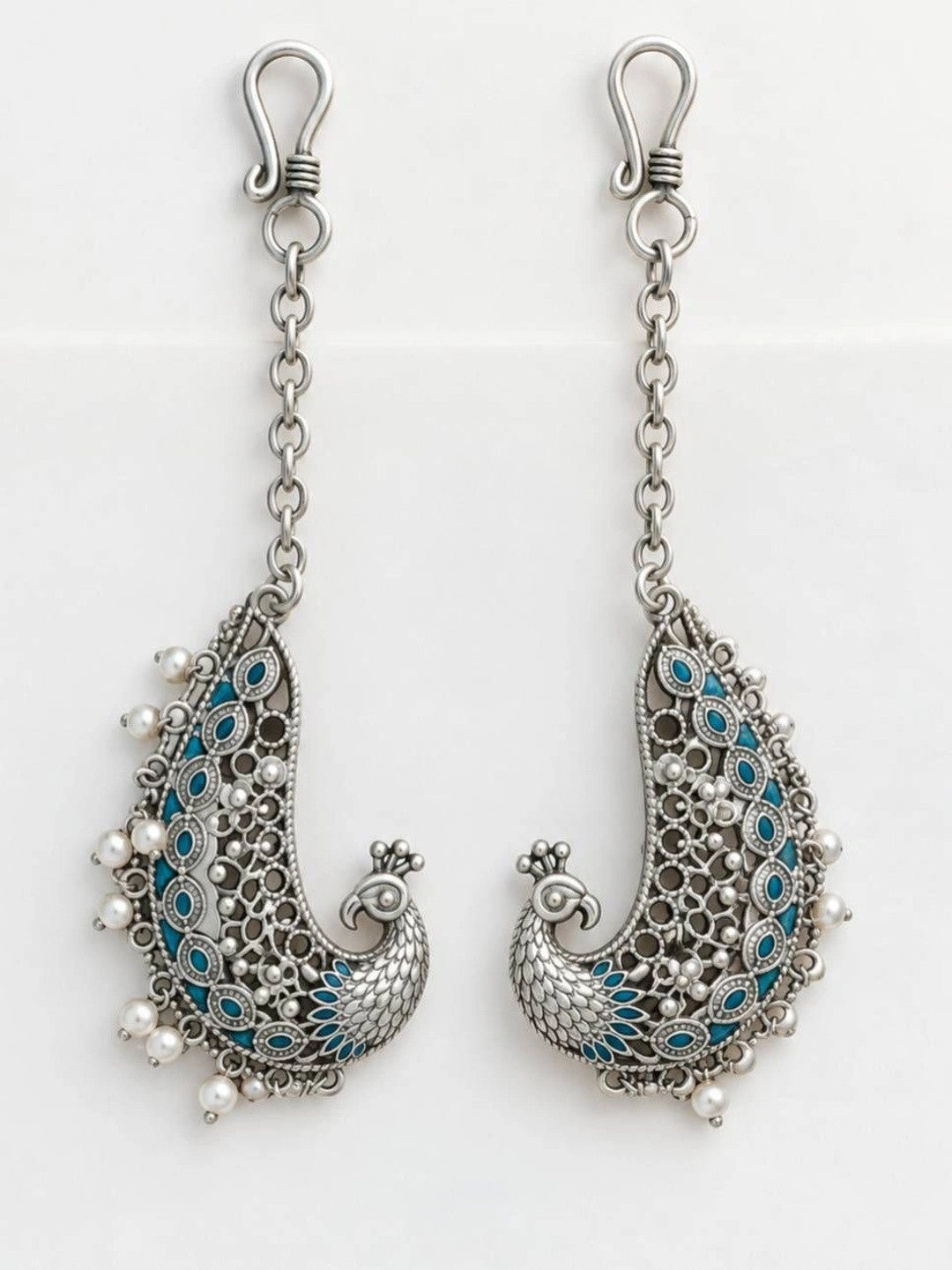 Pair of oxidised silver peacock ear cuffs with teal enamel laid flat on white background
