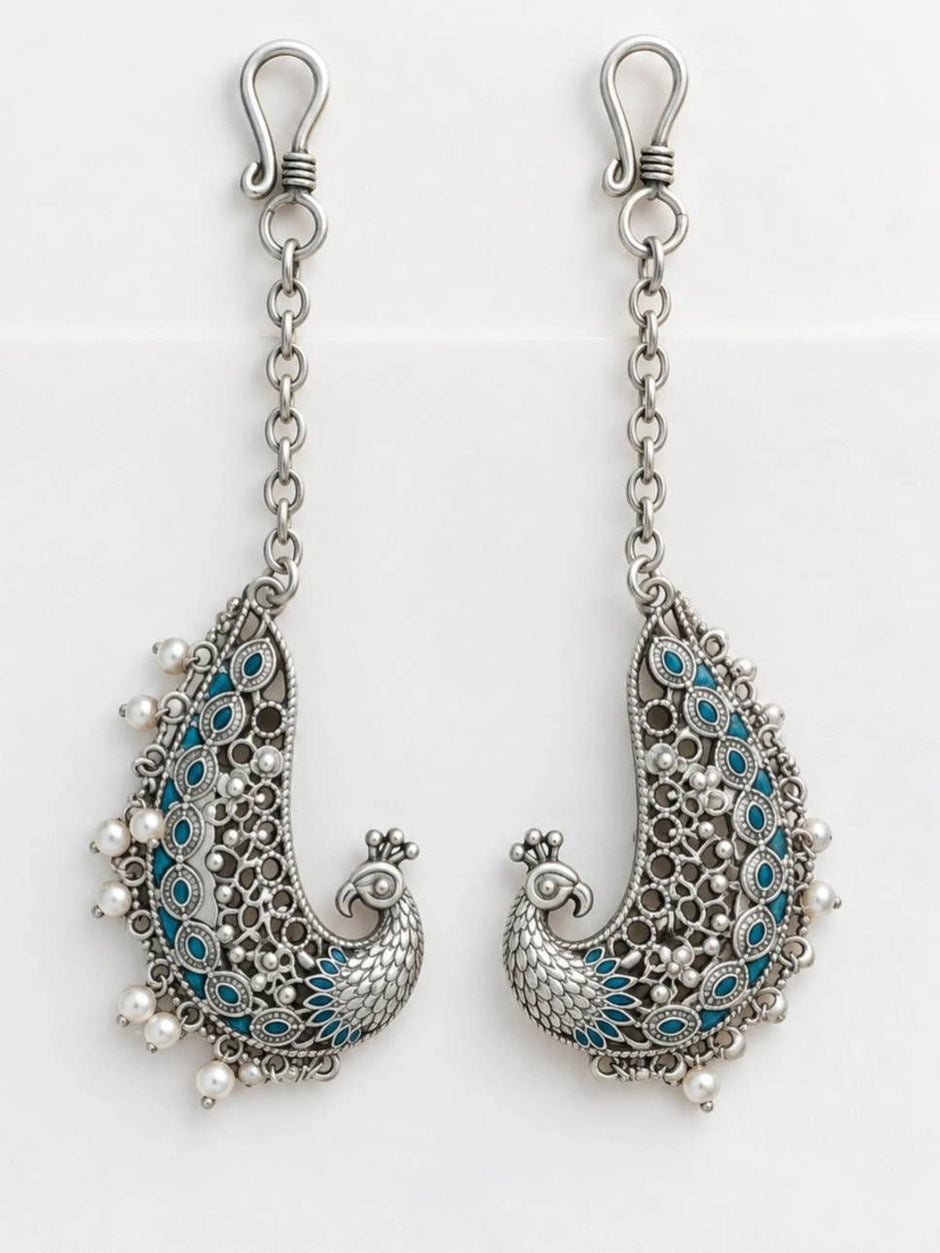 Pair of oxidised silver peacock ear cuffs with teal enamel laid flat on white background