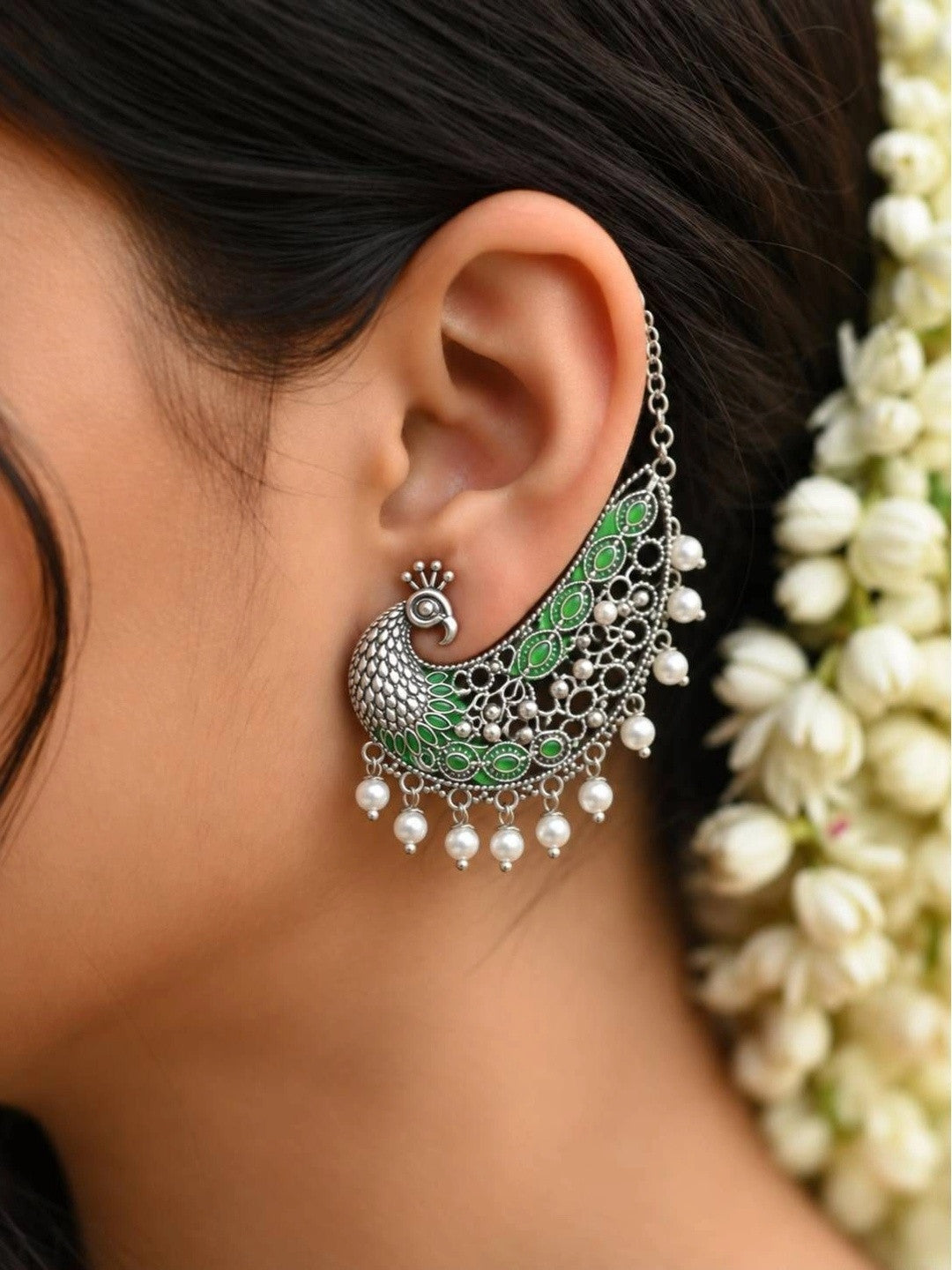 Peacock ear cuff worn on a woman's ear with jasmine flowers in hair showing full drape and pearl drop fringe