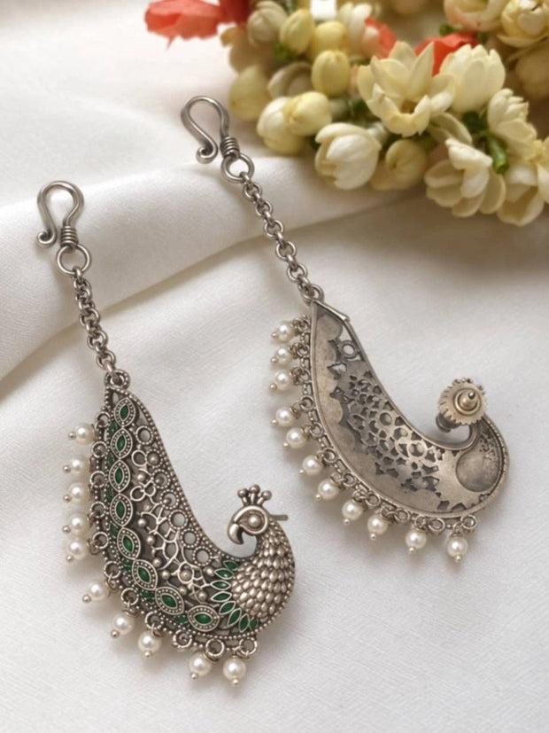 Pair of oxidised silver peacock ear cuff earrings with green enamel and pearl drops on white fabric