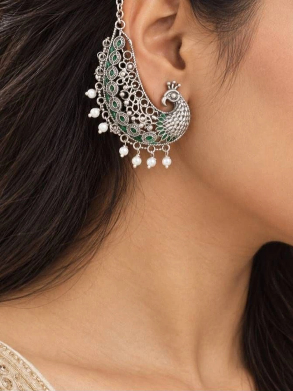 Oxidised silver peacock ear cuff earring worn on a woman's ear showing chain detail and green enamel